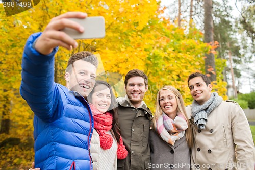 Image of smiling friends with smartphone in city park