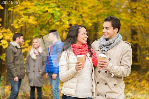 Image of group of smiling friend with coffee cups in park