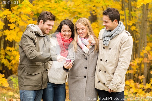 Image of smiling friends with smartphones in city park