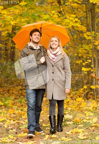 Image of smiling couple with umbrella in autumn park