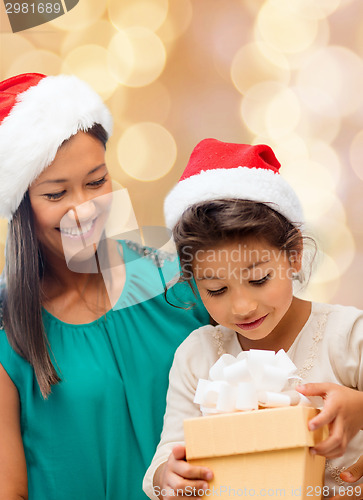 Image of happy mother and girl in santa hats with gift box