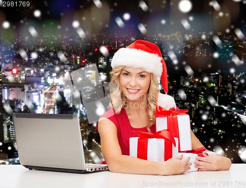 Image of smiling woman in santa hat with gifts and laptop