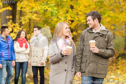 Image of group of smiling friend with coffee cups in park