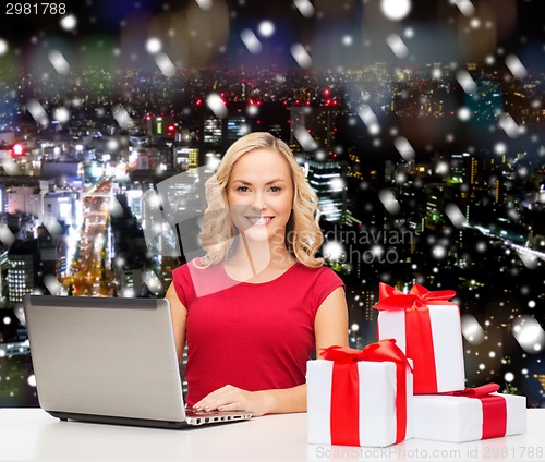 Image of smiling woman in red shirt with gifts and laptop