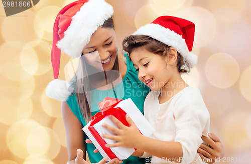 Image of happy mother and girl in santa hats with gift box