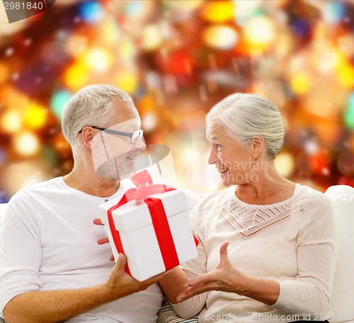 Image of happy senior couple with gift box at home