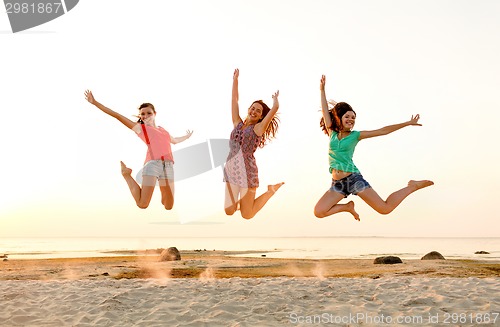 Image of smiling teen girls jumping on beach