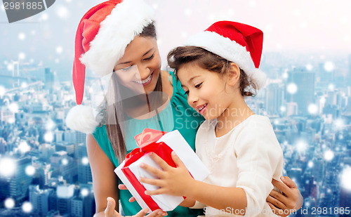 Image of happy mother and girl in santa hats with gift box