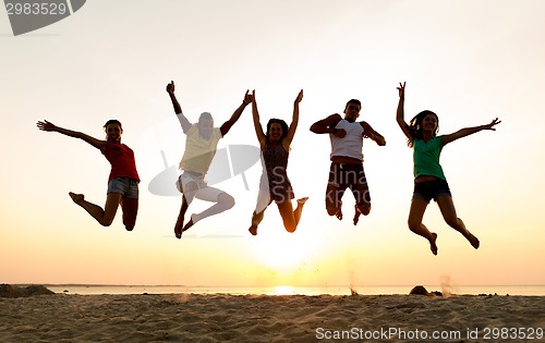 Image of smiling friends dancing and jumping on beach
