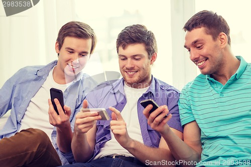 Image of smiling friends with smartphones at home