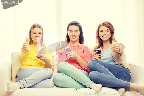 Image of smiling teenage girls with smartphones at home