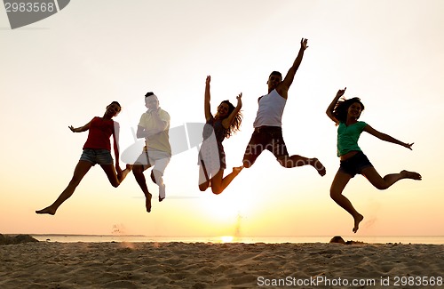 Image of smiling friends dancing and jumping on beach