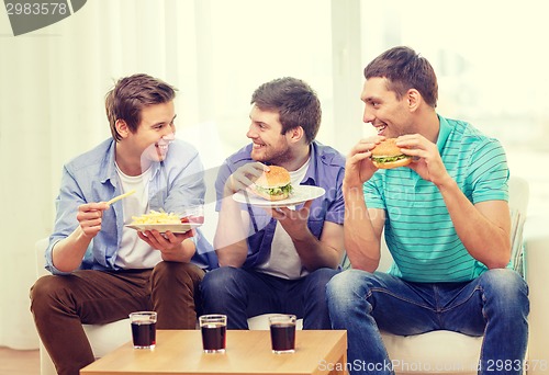 Image of smiling friends with soda and hamburgers at home