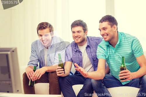 Image of happy male friends with beer watching tv at home