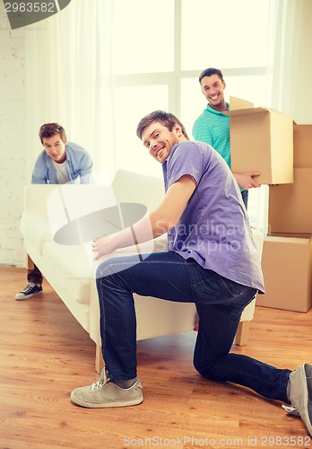 Image of smiling friends with sofa and boxes at new home