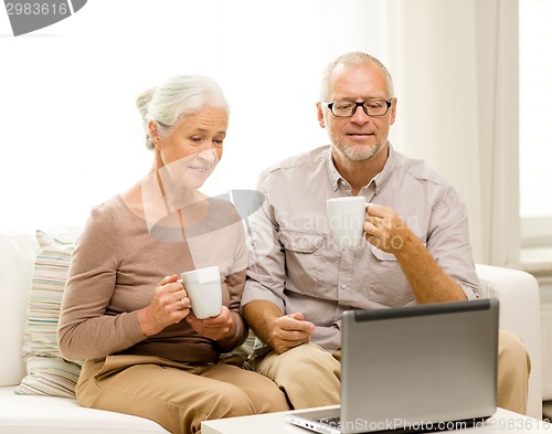 Image of happy senior couple with laptop and cups at home