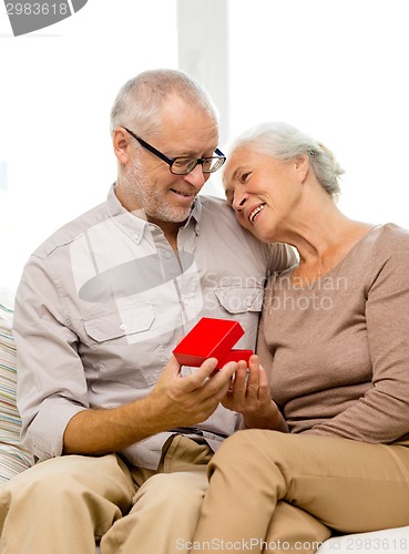 Image of happy senior couple with red gift box at home