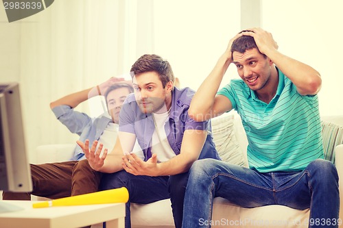 Image of sad male friends with vuvuzela watching sports