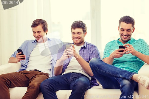 Image of smiling friends with smartphones at home