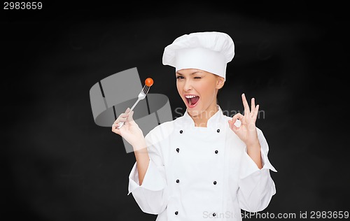 Image of smiling female chef with fork and tomato