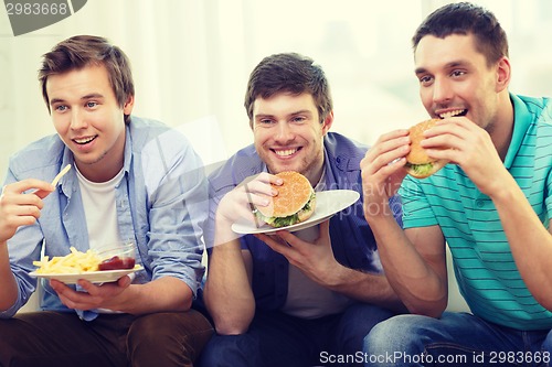 Image of smiling friends with soda and hamburgers at home