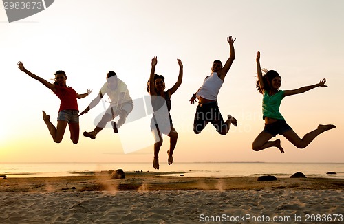 Image of smiling friends dancing and jumping on beach
