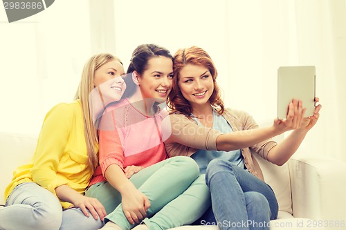 Image of three smiling teenage girls with tablet pc at home