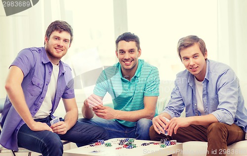 Image of happy three male friends playing poker at home