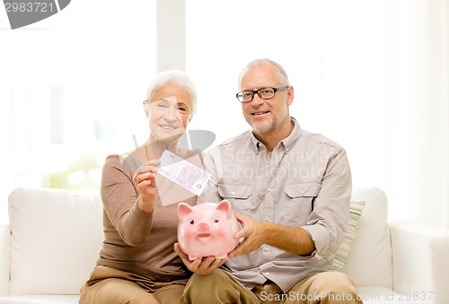 Image of senior couple with money and piggy bank at home