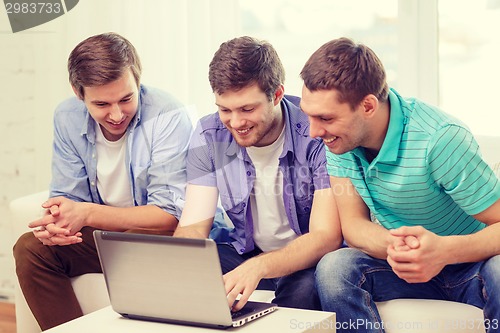 Image of smiling friends with laptop computer at home