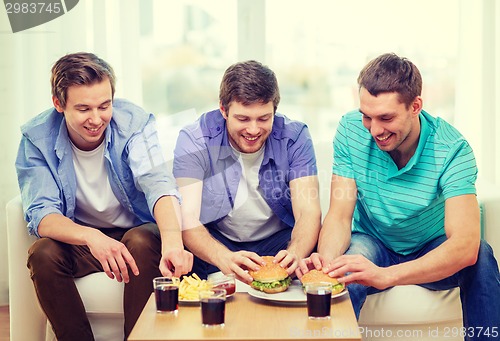 Image of smiling friends with soda and hamburgers at home