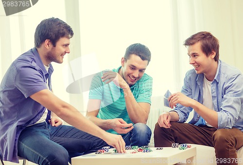 Image of happy three male friends playing poker at home