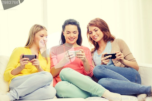 Image of smiling teenage girls with smartphones at home