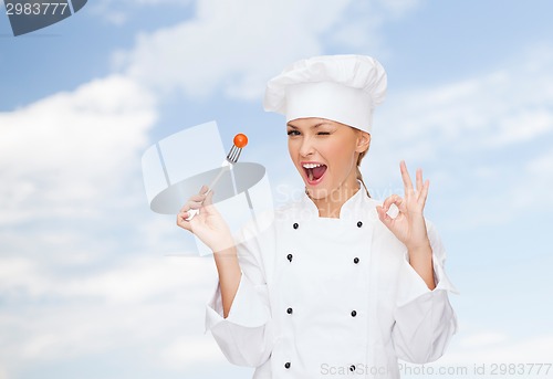 Image of smiling female chef with fork and tomato