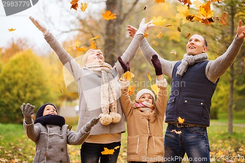 Image of happy family playing with autumn leaves in park