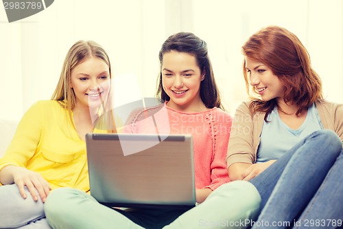 Image of three smiling teenage girls with laptop at home