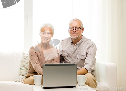 Image of happy senior couple with laptop and cups at home