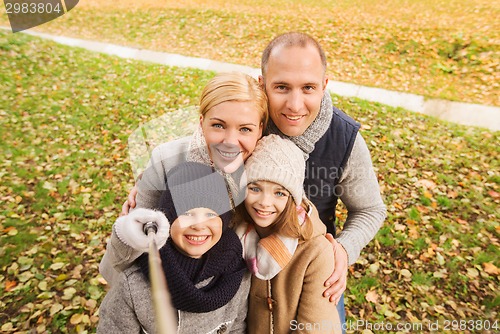 Image of happy family with selfie stick in autumn park