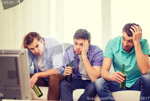 Image of sad male friends with beer watching sports