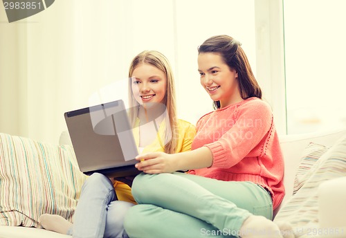 Image of two smiling teenage girls with laptop at home