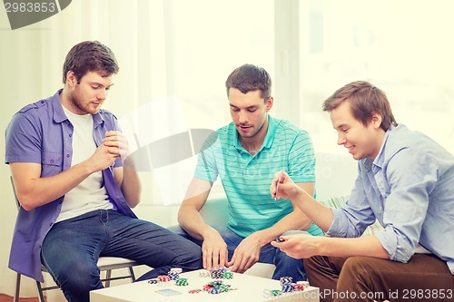 Image of happy three male friends playing poker at home