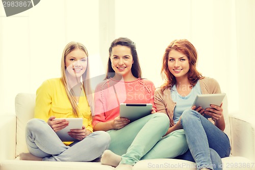 Image of three smiling teenage girls with tablet pc at home