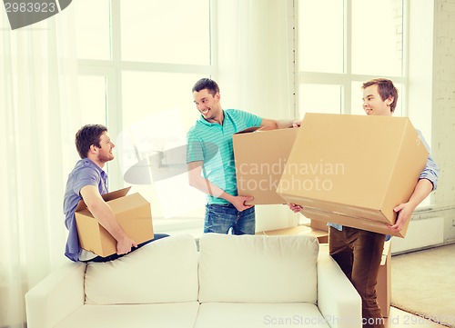 Image of smiling male friends carrying boxes at new place