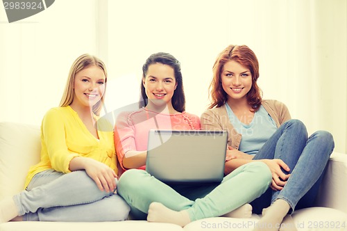 Image of three smiling teenage girls with laptop at home