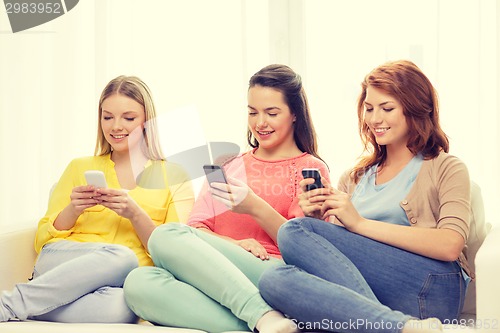Image of smiling teenage girls with smartphones at home