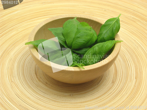 Image of Wooden bowl with basil on bamboo plate