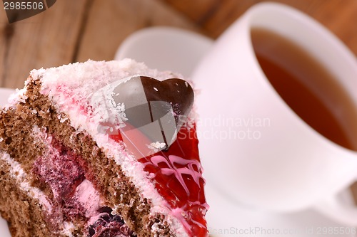 Image of Piece of cake with chocolate heart on wooden background