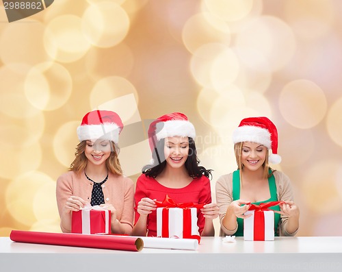Image of smiling women in santa helper hats packing gifts