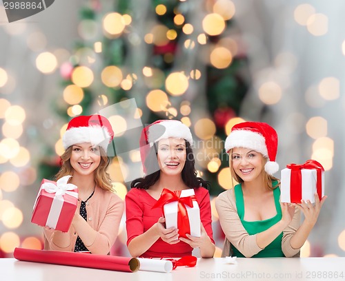 Image of smiling women in santa helper hats packing gifts