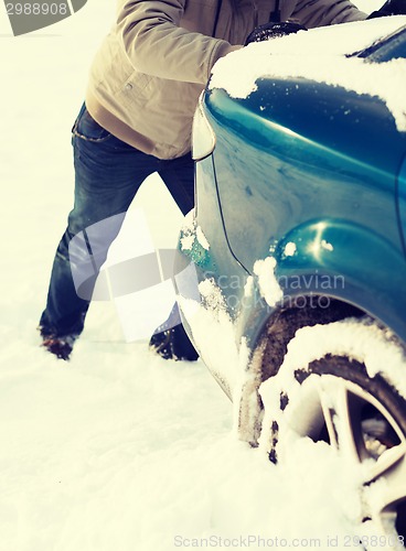 Image of closeup of man pushing car stuck in snow